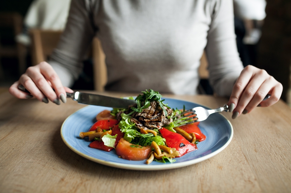 Person using a knife and fork to eat dysphagia diet textured food from a blue plate